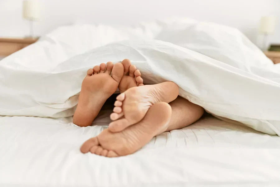 A man and woman’s feet peeking out from under a blanket during sex.